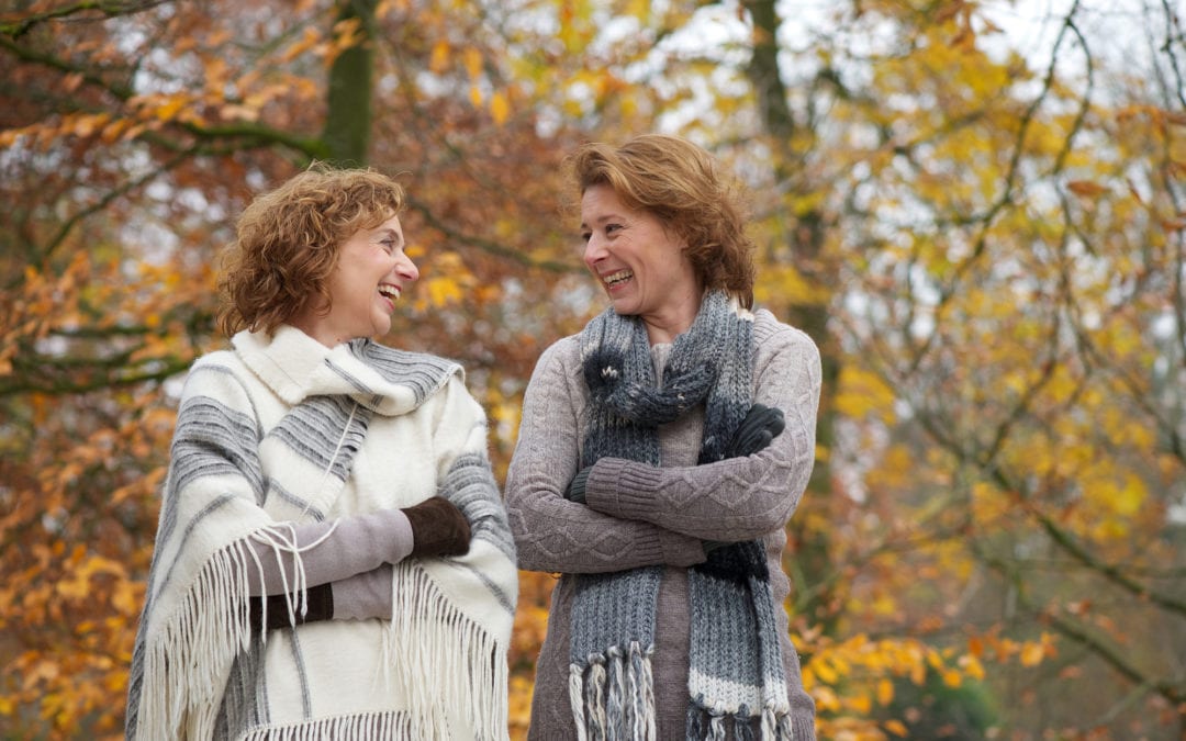 Mature friends smiling at eachother in a park in autumn